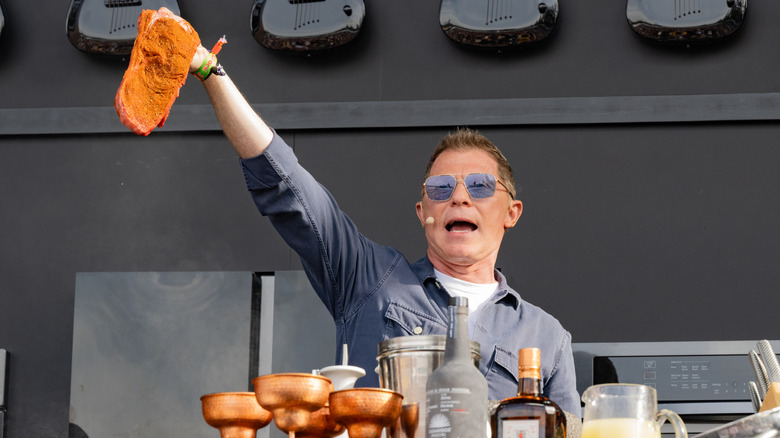 Celebrity chef Bobby Flay holds up a steak on stage at an event.