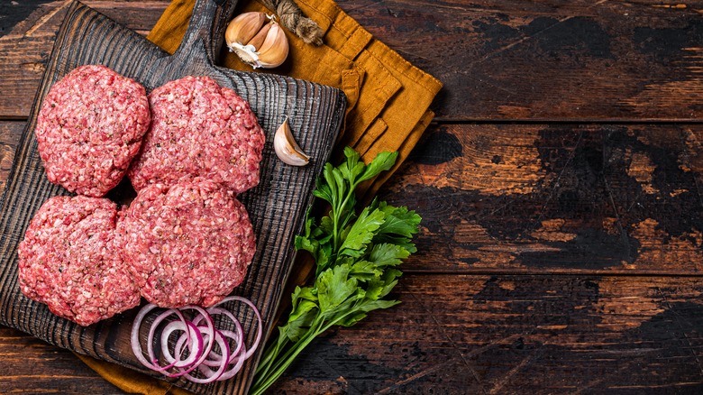 Four uncooked burger parries rest on a wooden board in a rustic setting.