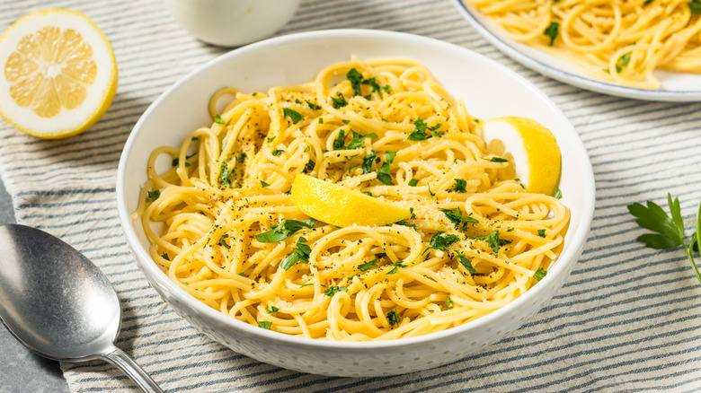 White bowl of pasta with herbs and lemon on a striped tablecloth