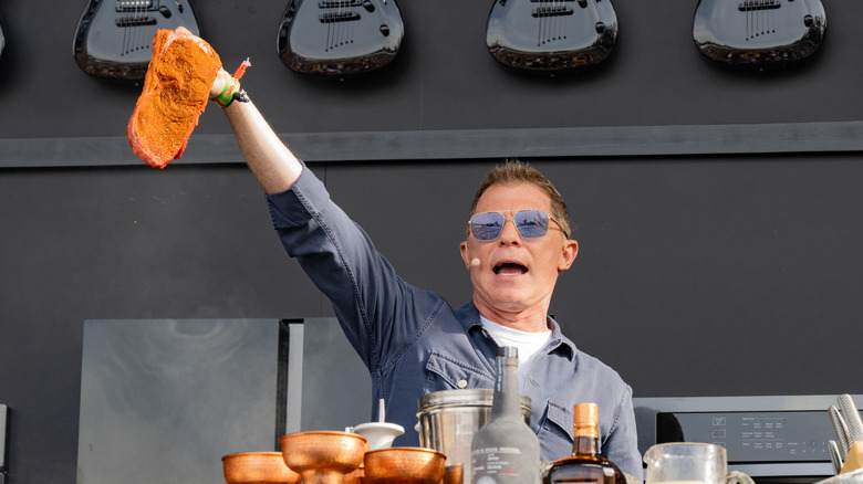 Bobby Flay holding a seasoned steak up at a cooking demonstration.