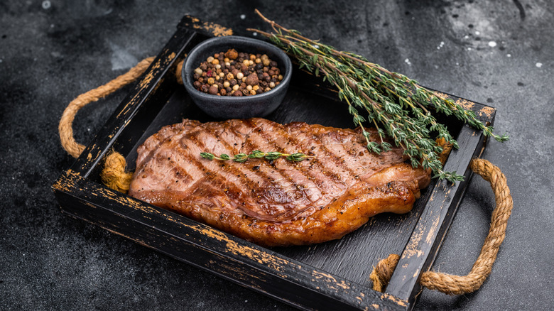 Grilled New York strip steak on a tray with herbs and spices.