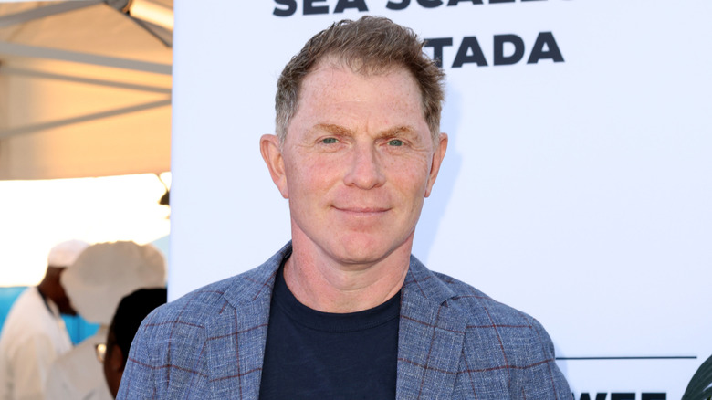 Bobby Flay smiling in front of sponsored board.