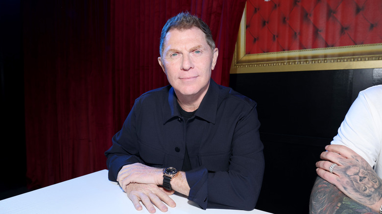 Celebrity chef Bobby Flay is pictured at a restaurant table with a red curtain in the background.
