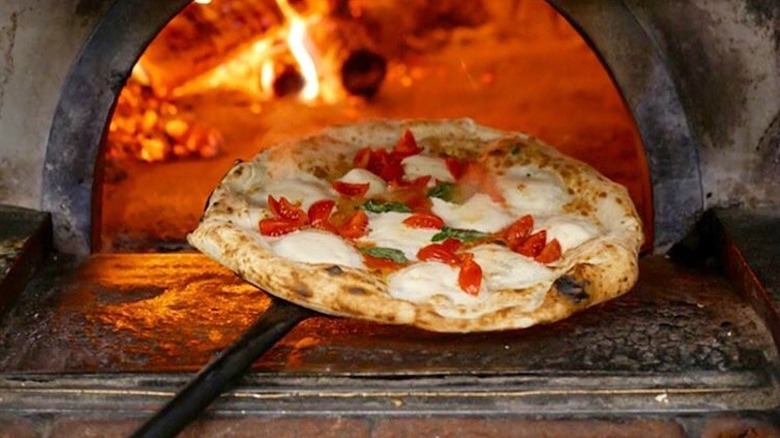 A margherita pizza being taken out of a wood burning oven at Pizzeria Da Attilio in Naples