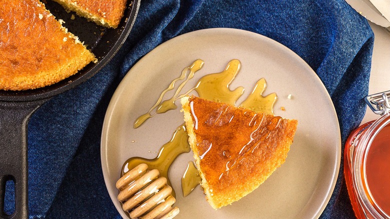 A piece of cornbread drizzled with honey on a cream-colored plate