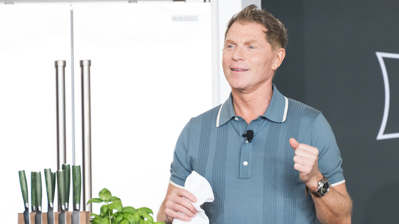 Bobby Flay in light blue polo shirt holding a napkin and standing next to a set of green-handled knives