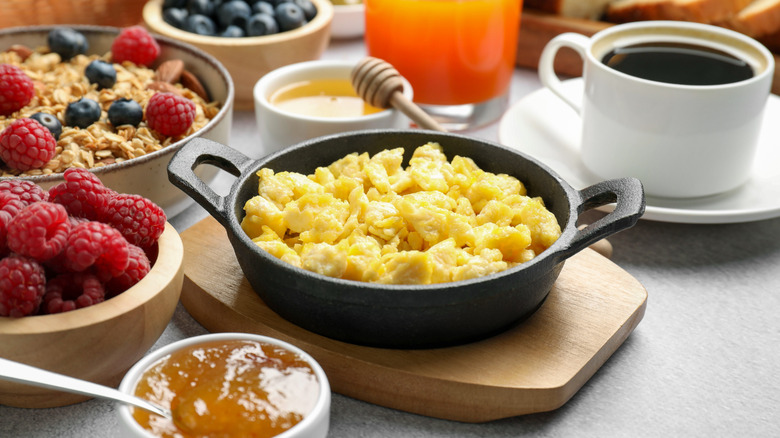 A small castiron pan of scrambled eggs with coffee, fruit, granola, and jam