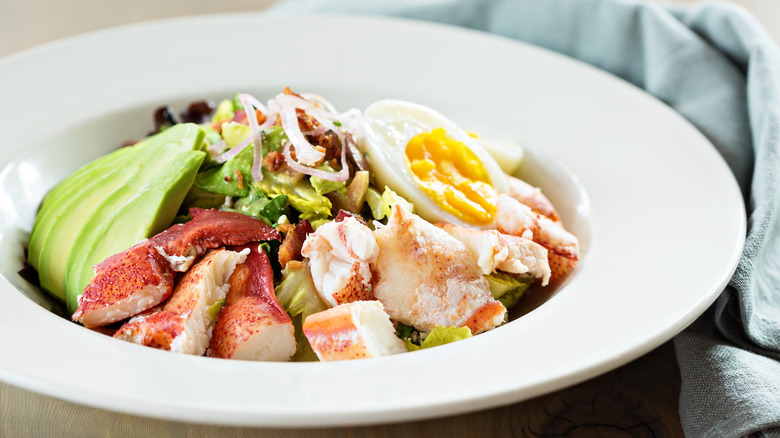 A lovely Cobb salad with lobster instead of chicken in a shallow white bowl.