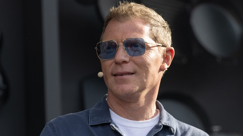 Bobby Flay smiling wearing blue-tinted sunglasses and a blue button-down shirt