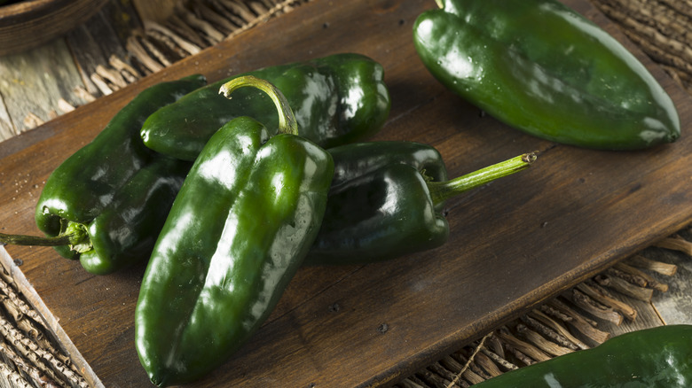 Fresh green poblano peppers are arranged on s wooden tray.