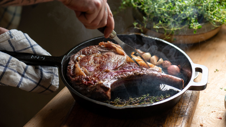 A large steak has been seared in a cast iron pan.