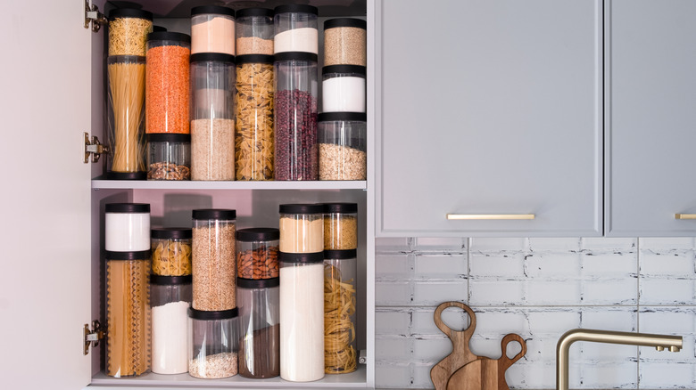 A kitchen pantry is organized with cylindrical plastic jar for storing loose products