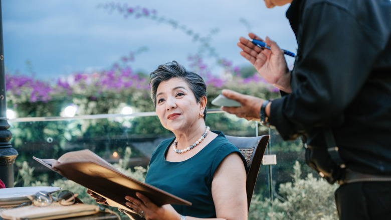 Waiter explaining something to a woman holding a menu