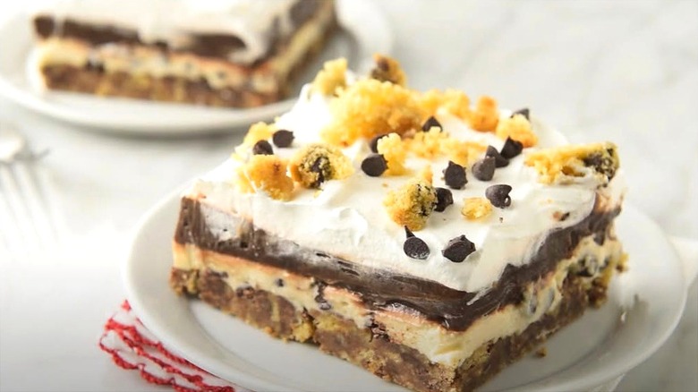 Serving of chocolate lush dessert topped with crumbled shortbread crust and chocolate chips on a white plate