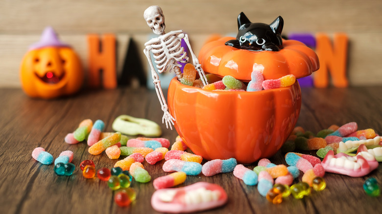 A ceramic pumpkin filled with candy and a skeleton.