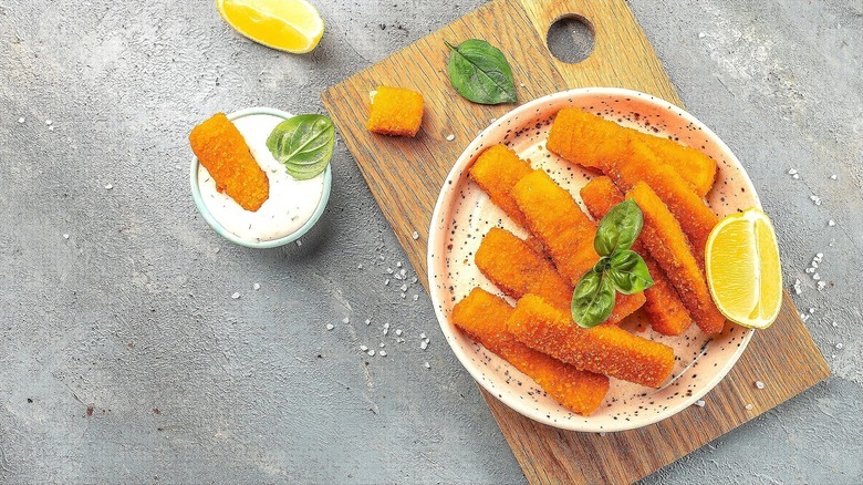 Fish sticks in a bowl with lemon over a wooden serving board