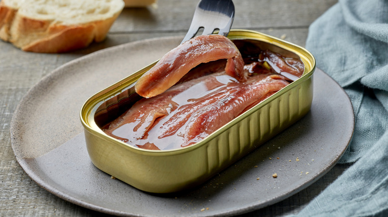 A fork lifts and anchovy out of its tin.
