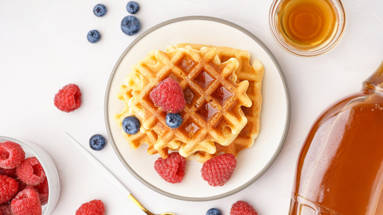 A plate of waffles with berries and maple syrup