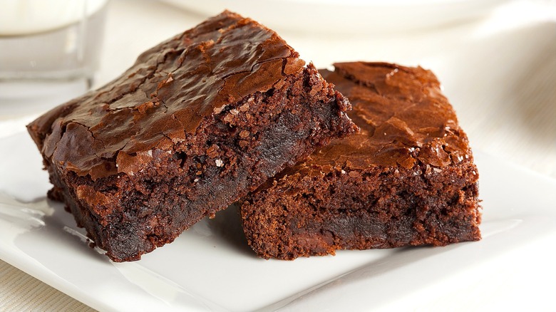 Closeup of two chocolate brownies partially-stacked together sit on a white plate