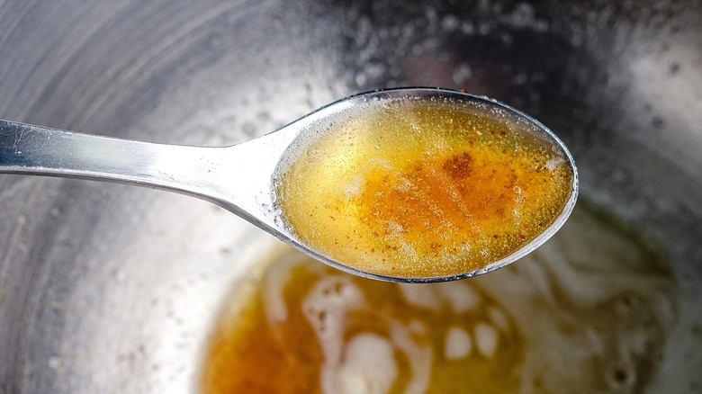 Brown butter bubbles on a metal spoon over a large metal bowl