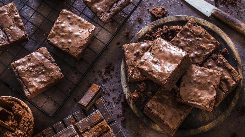 Brownies stacked in a bowl and on a cooling rach with cocoa powder and dark chocolate squares