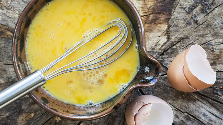 raw beaten eggs in a bowl with whisk