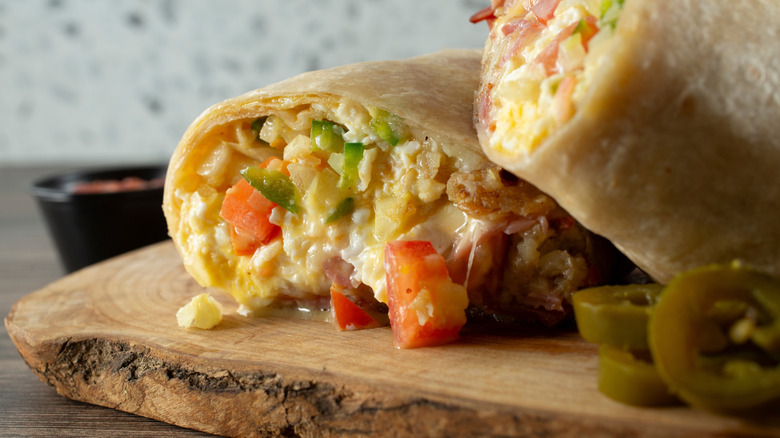 two breakfast burritos on a wooden cutting board
