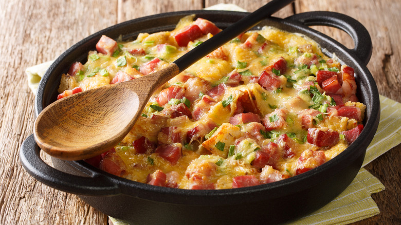 Egg based breakfast casserole in a pan with a wooden spoon sitting on top