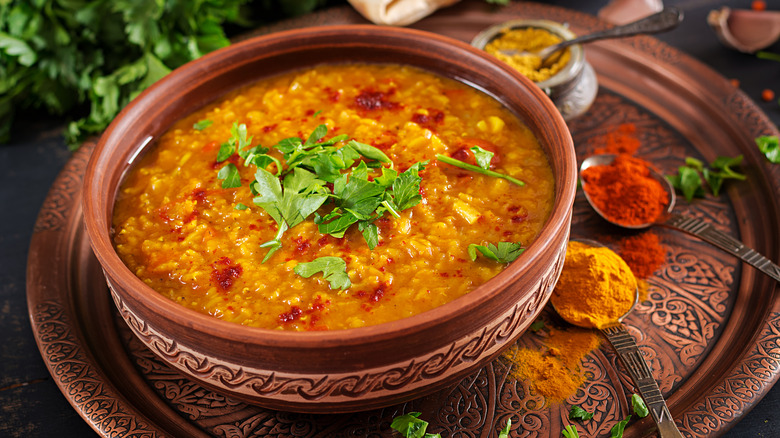 dal with parsley on top in a ceramic bowl next to spices