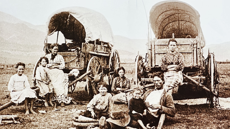 Sepia-and-white photo of families sitting outside of covered wagons in a field.