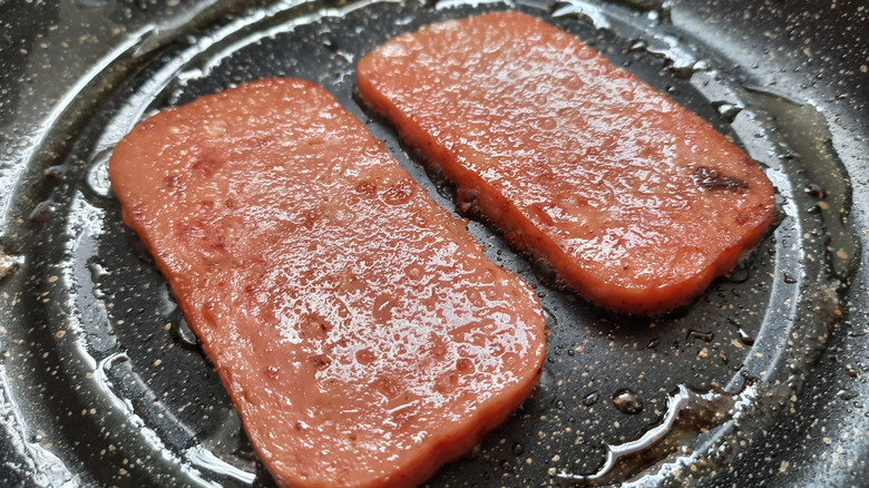 two pieces of spam frying in pan