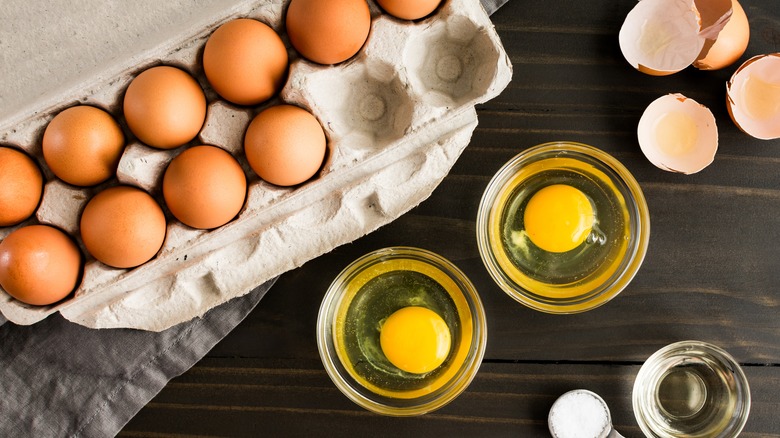 A carton of eggs with two cracked into small glass bowls.