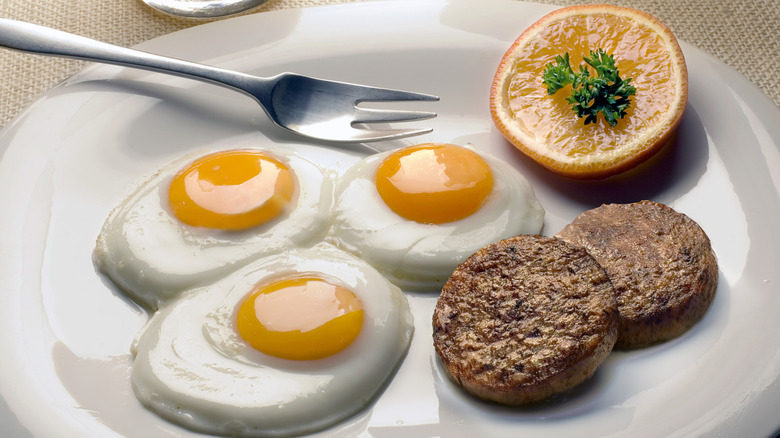 Round breakfast sausage is plated with three sunny eggs