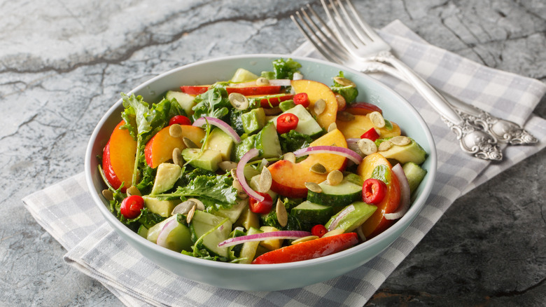 salad in a bowl with onions, peaches, seeds, and forks beside