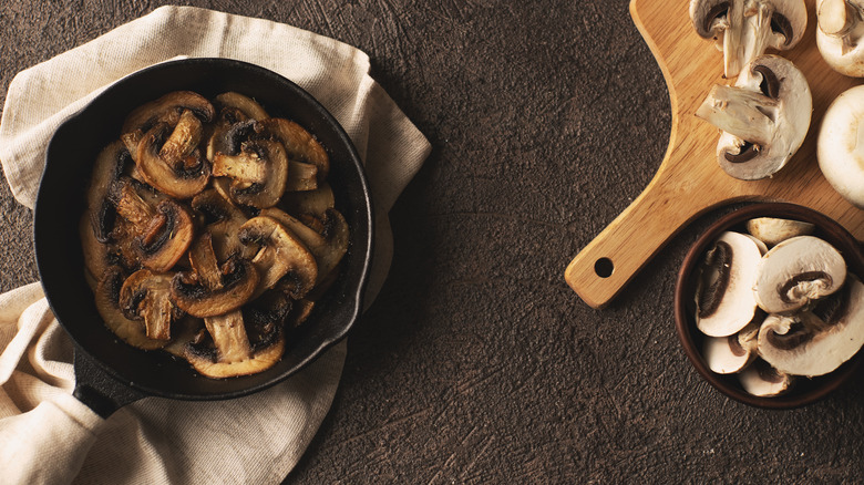 Sliced mushrooms in a cast iron pan, in a small bowl, and on a cutting board