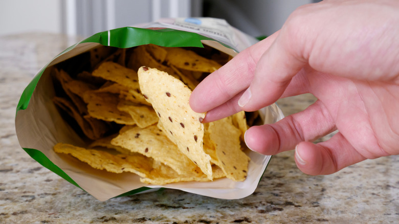 Person grabbing a tortilla chip from an open bag on kitchen counter