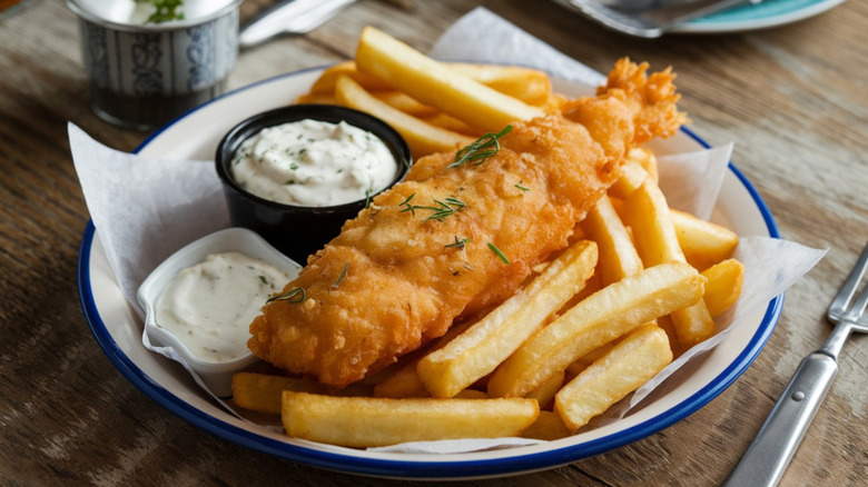 Fried fish and chips in a plate with bowls of dips