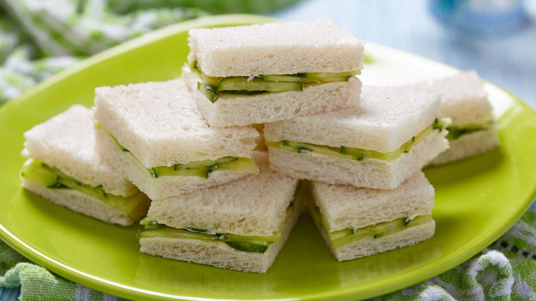 A green plate with a stack of crustless cucumber sandwiches.