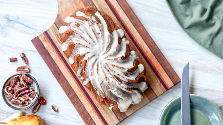 Brown butter bourbon loaf cake on cutting board with pecans and knife