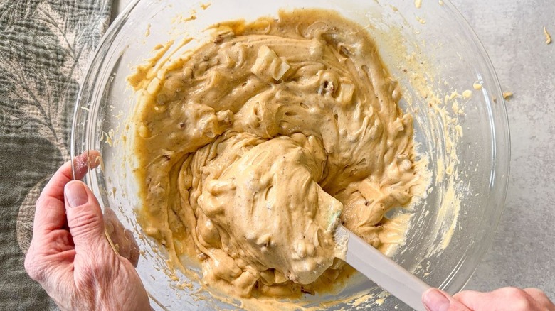 Stirring chopped pears and pecans into brown butter bourbon loaf cake batter in glass bowl with rubber spatula