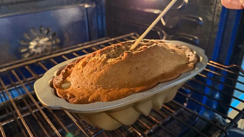 Inserting wooden skewer into brown butter bourbon loaf cake in loaf pan in oven