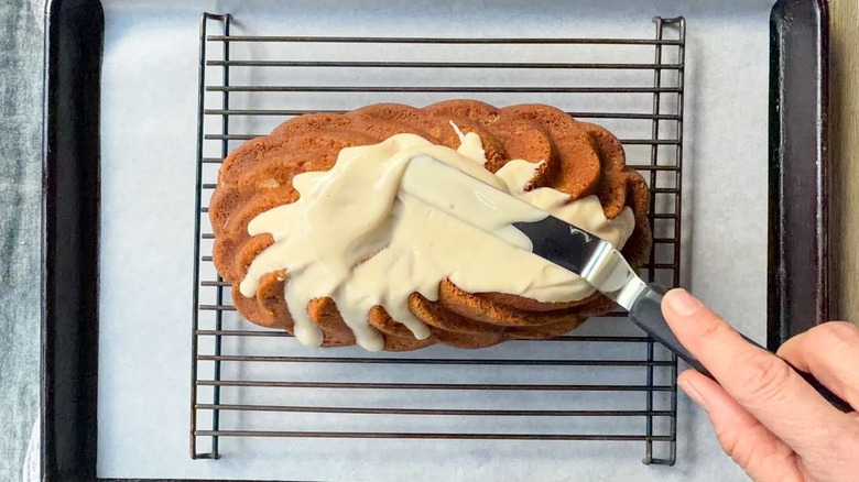 Spreading glaze over brown butter bourbon loaf cake on rack set over baking sheet with parchment