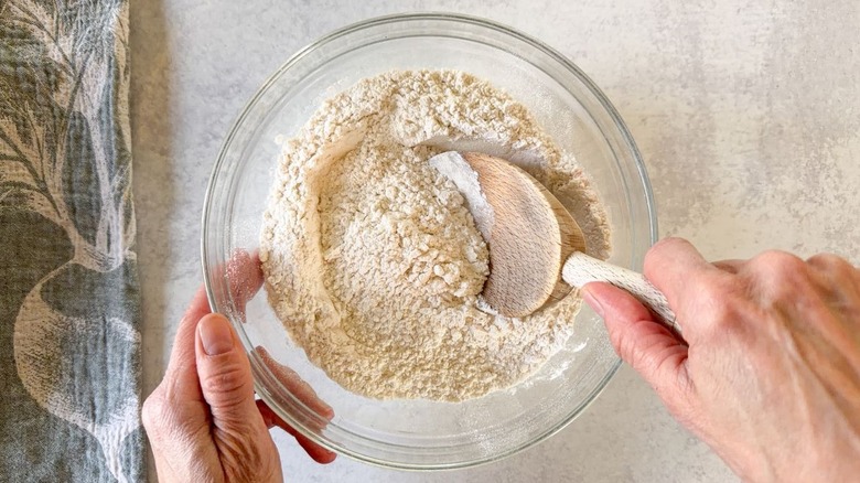Stirring dry ingredients for brown butter bourbon loaf cake in glass bowl with wooden spoon