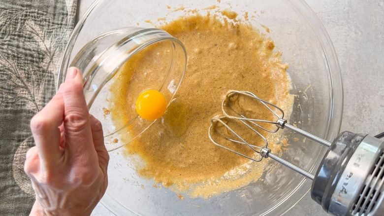 Adding eggs to brown butter bourbon loaf cake batter in glass bowl
