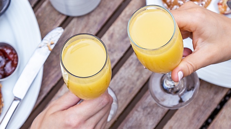 Two people toasting with mimosas at brunch
