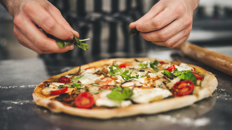 Hands adding arugula to pizza