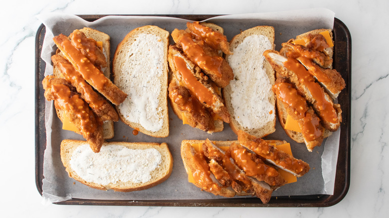 Multiple bread slices containing slices of cheddar cheese and sliced chicken tenders drizzled with buffalo sauce.