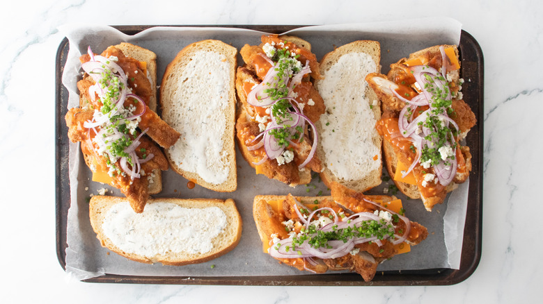 Multiple bread slices containing cheddar, chicken, blue cheese crumbles, onion, and chives.
