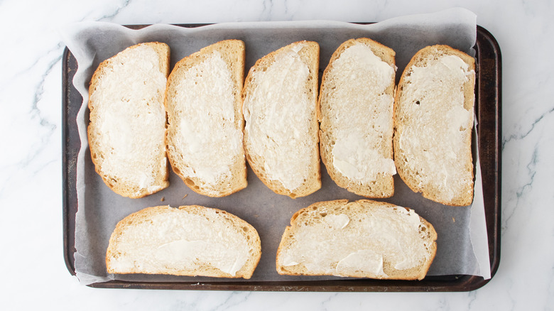 A large baking sheet lined with wax paper containing buttered bread slices.