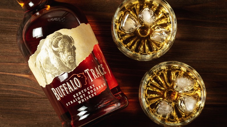 a bottle of buffalo trace bourbon on a wooden table next to two filled glasses